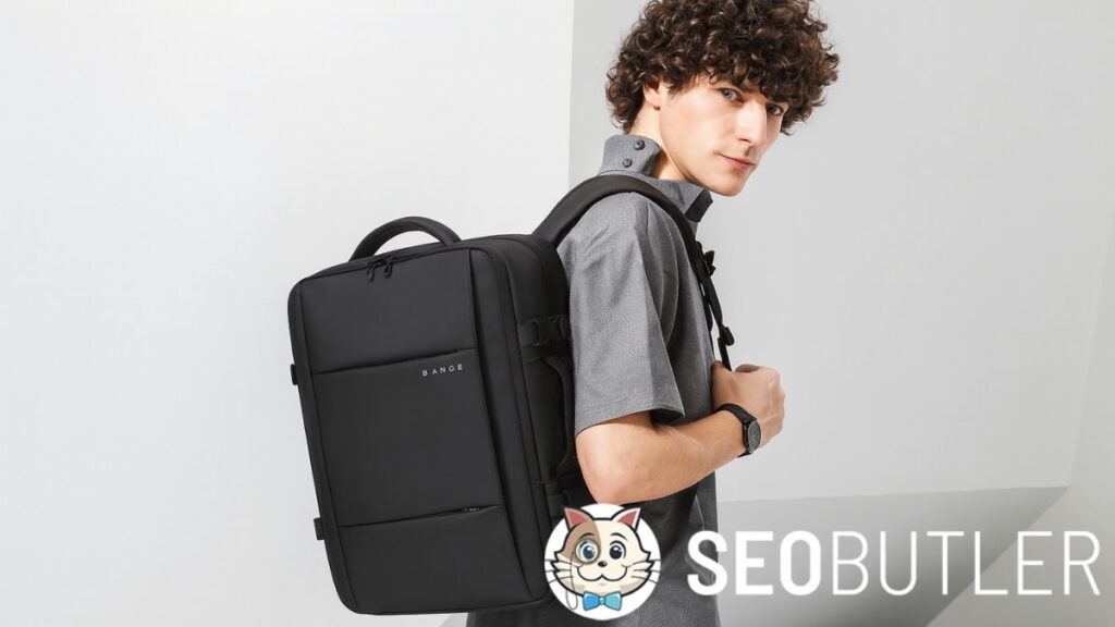 A young man with curly brown hair wears a gray short-sleeve button-up shirt and carries a large, black rectangular BANGE backpack on his back. He looks over his shoulder while standing indoors against a minimalist white and gray background.