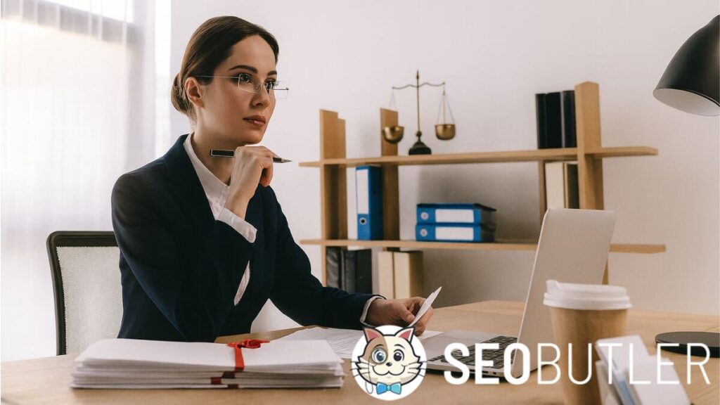 A professional woman in a navy suit sits at a desk with a laptop, holding papers and a pen, with scales of justice and bookshelves in the background.