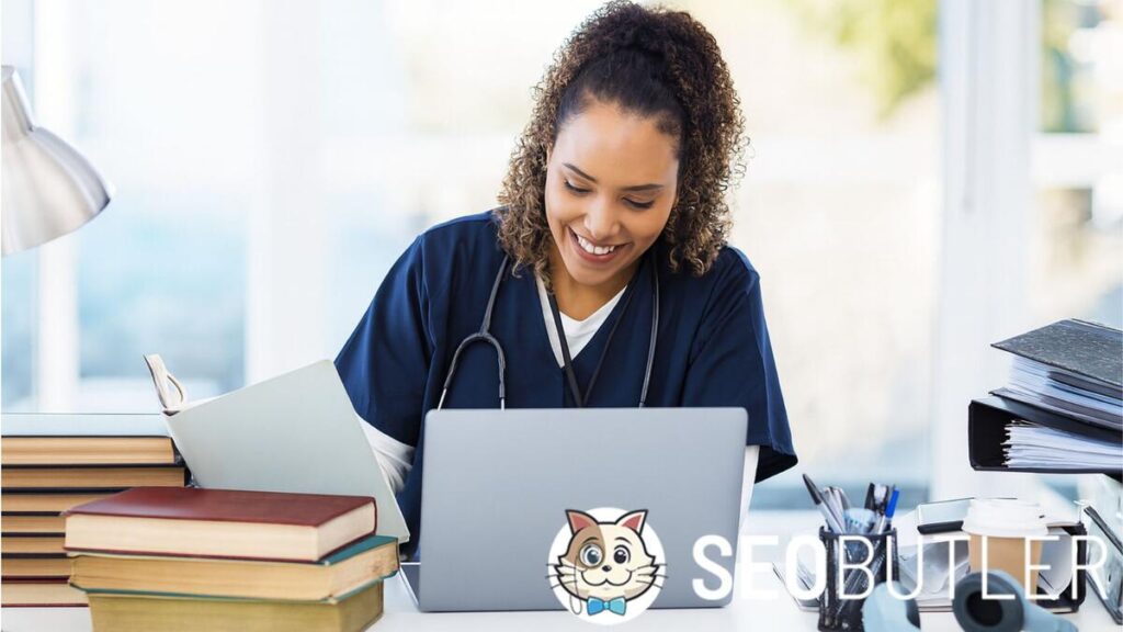 Medical student in navy scrubs with a stethoscope studying at a desk, using a laptop with textbooks, coffee, and study materials around her.