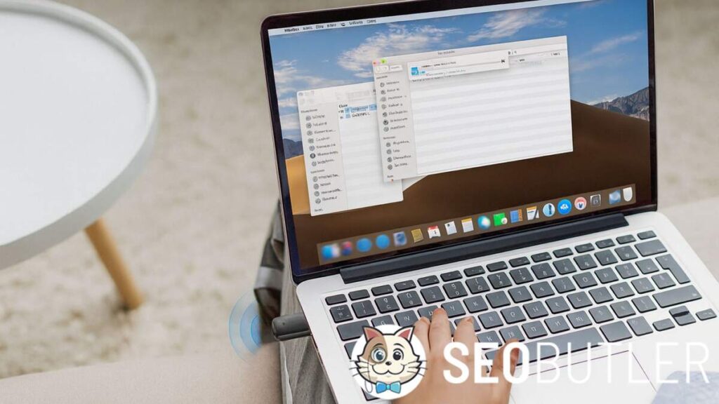 A person sits on a beige sofa using a silver MacBook Pro with a Wi-Fi USB adapter plugged into the side. Their left hand rests on the keyboard, while the laptop screen shows macOS Finder windows with a file transfer in progress. A small white round table is visible in the background.